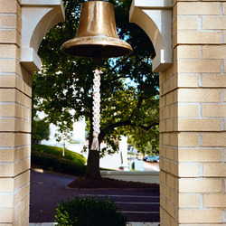 A bronze bell hanging in a yellow brick frame.