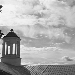 A building and tree in front of a cloudy sky.