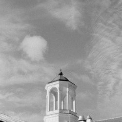 A cupola on top of a roof in front of a blue sky with wispy clouds.