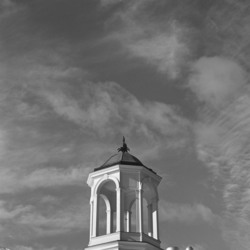A cupola on top of a roof in front of a blue sky with wispy clouds.